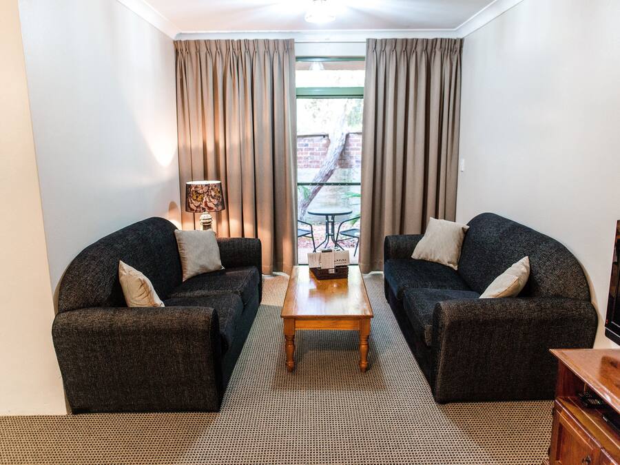 A compact living room with two dark sofas, a wooden coffee table, and a TV stand.