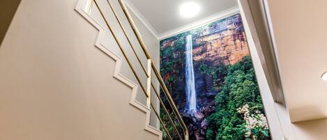 A staircase with a railing leading to a room with a large wall mural of a waterfall.
