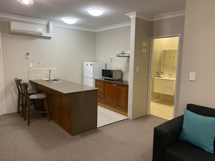 A compact kitchen with a central island, bar stools, a refrigerator, microwave, and a sink.