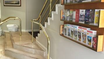 A staircase with gold railings leading to an upper floor, a wall-mounted display of travel brochures, and a framed picture on the wall.
