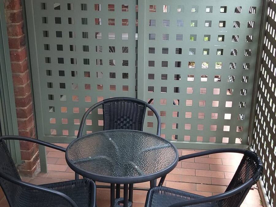 A patio area with a round table and four chairs, a green metal fence, and a brick wall.