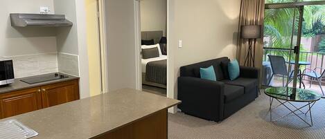 Ein kleines Hotelzimmer mit einer Küchenzeile, einem Sofa mit Kissen, einem kleinen Tisch und einem Balkon mit Stühlen.