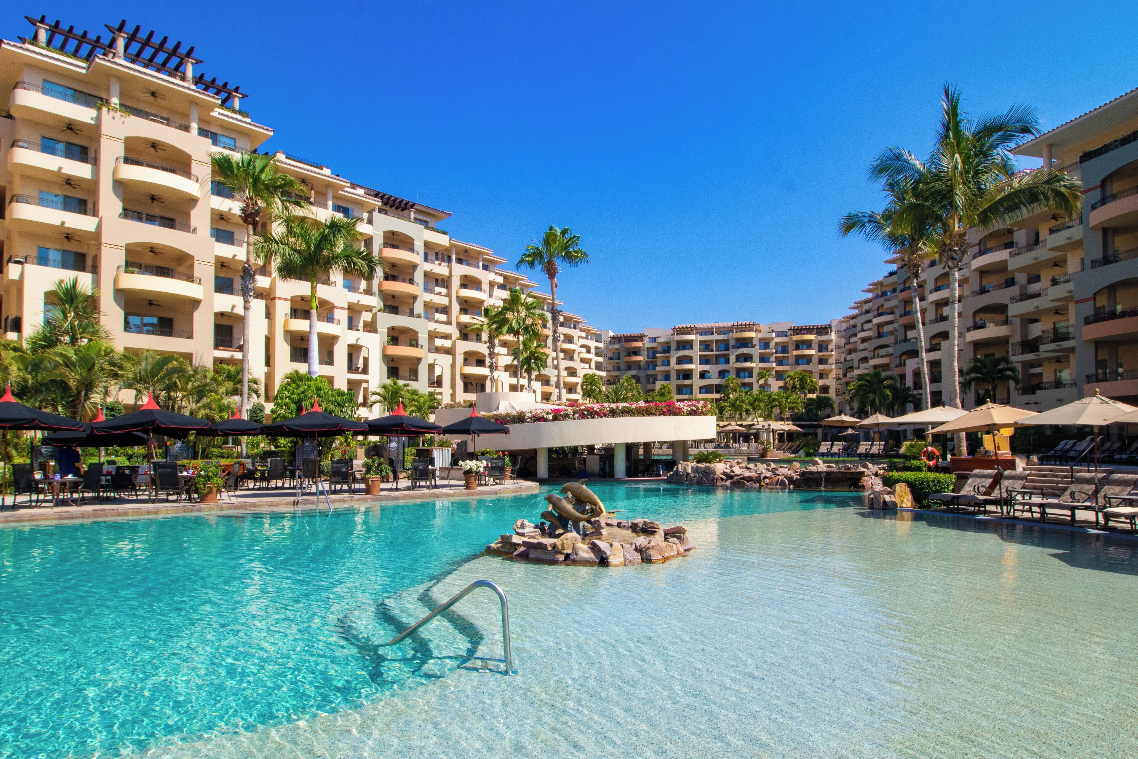 Un hotel con una piscina grande, palmeras y varios balcones.