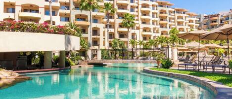 A hotel with a large pool surrounded by palm trees and lounge chairs.
