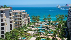 Een resort met meerdere gebouwen, een zwembad en uitzicht op de oceaan en een cruiseschip.