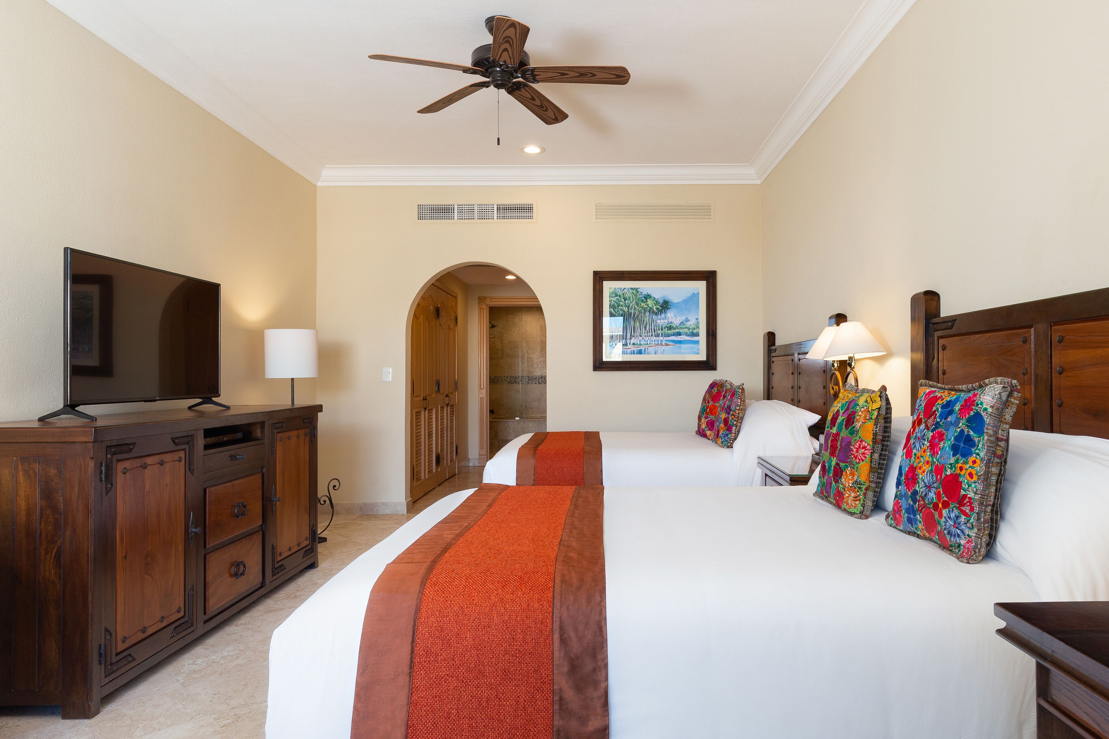 A hotel room with a large bed, a TV, a desk, and a ceiling fan.