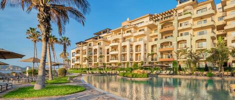 A hotel with multiple balconies, a swimming pool, and palm trees.