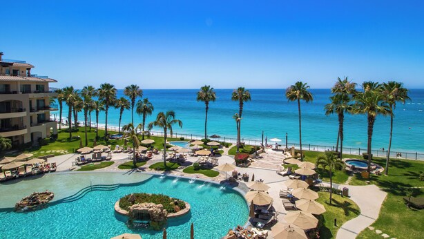 Een resort met een groot zwembad, palmbomen en uitzicht op de oceaan.