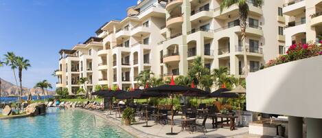 Un hotel con piscina, mobiliario exterior y balcones.