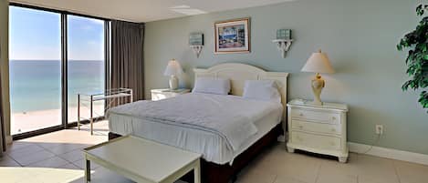 A bedroom with a bed, bedside tables, a nightstand, a bench, and a view of the ocean.