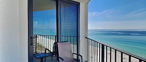 Un balcon avec une porte vitrée, deux chaises et une vue sur l’océan.