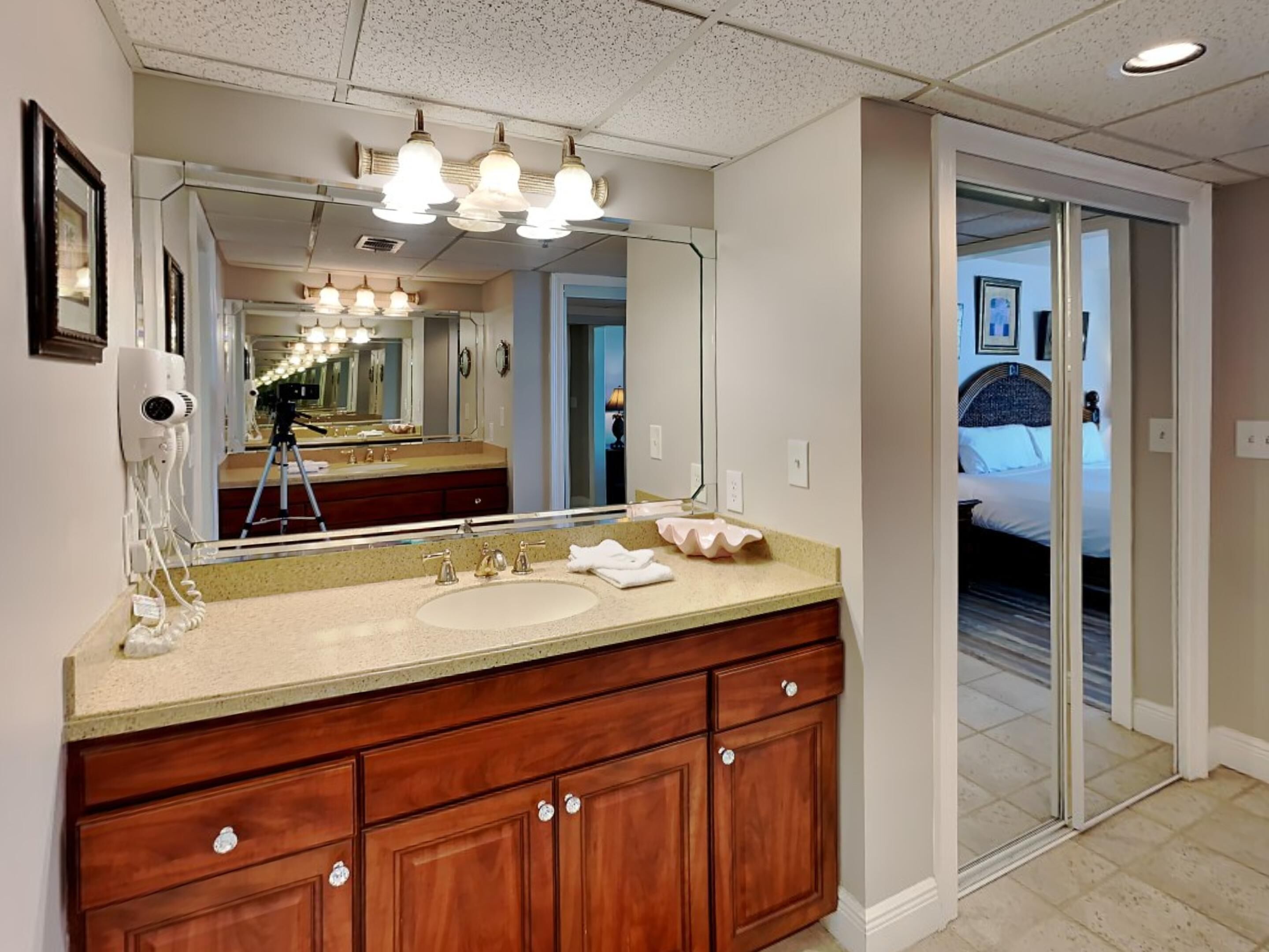 A bathroom with a large mirror, two sinks, wooden cabinets, and a ceiling light fixture.