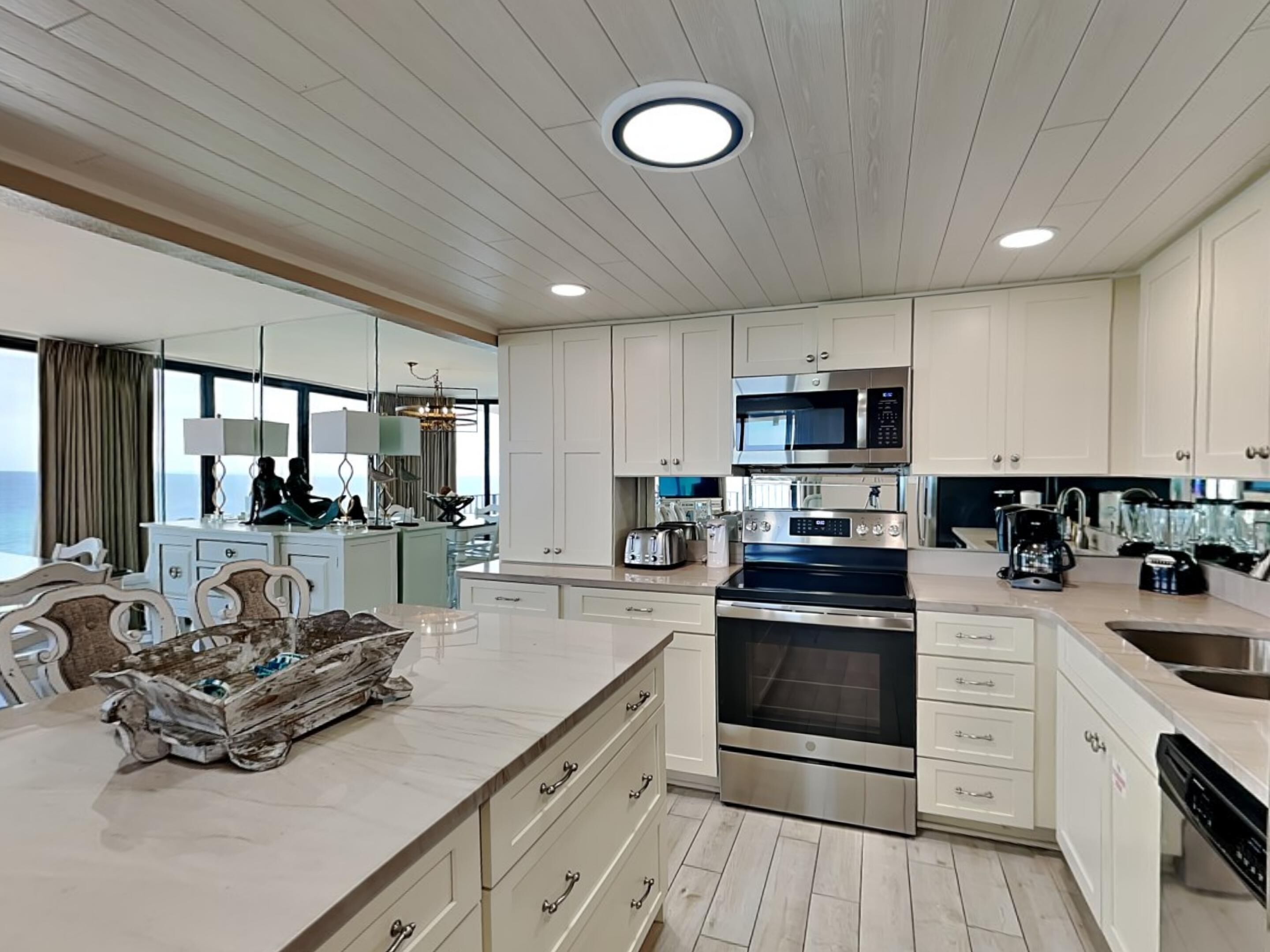 A modern kitchen with white cabinetry, stainless steel appliances, and a large island with a marble countertop.