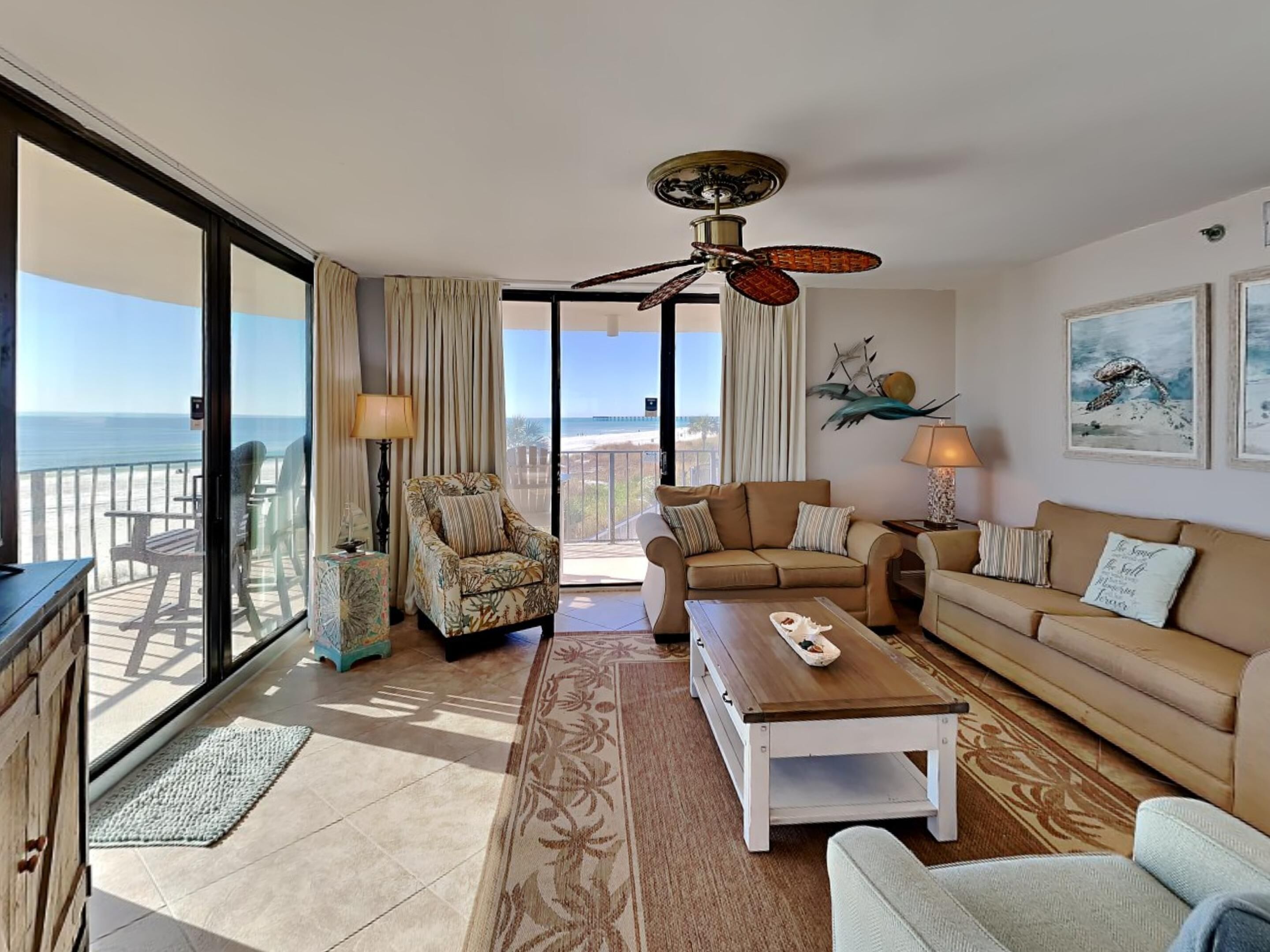 A spacious living room with a balcony overlooking the sea, furnished with a sofa, armchairs, and a coffee table.