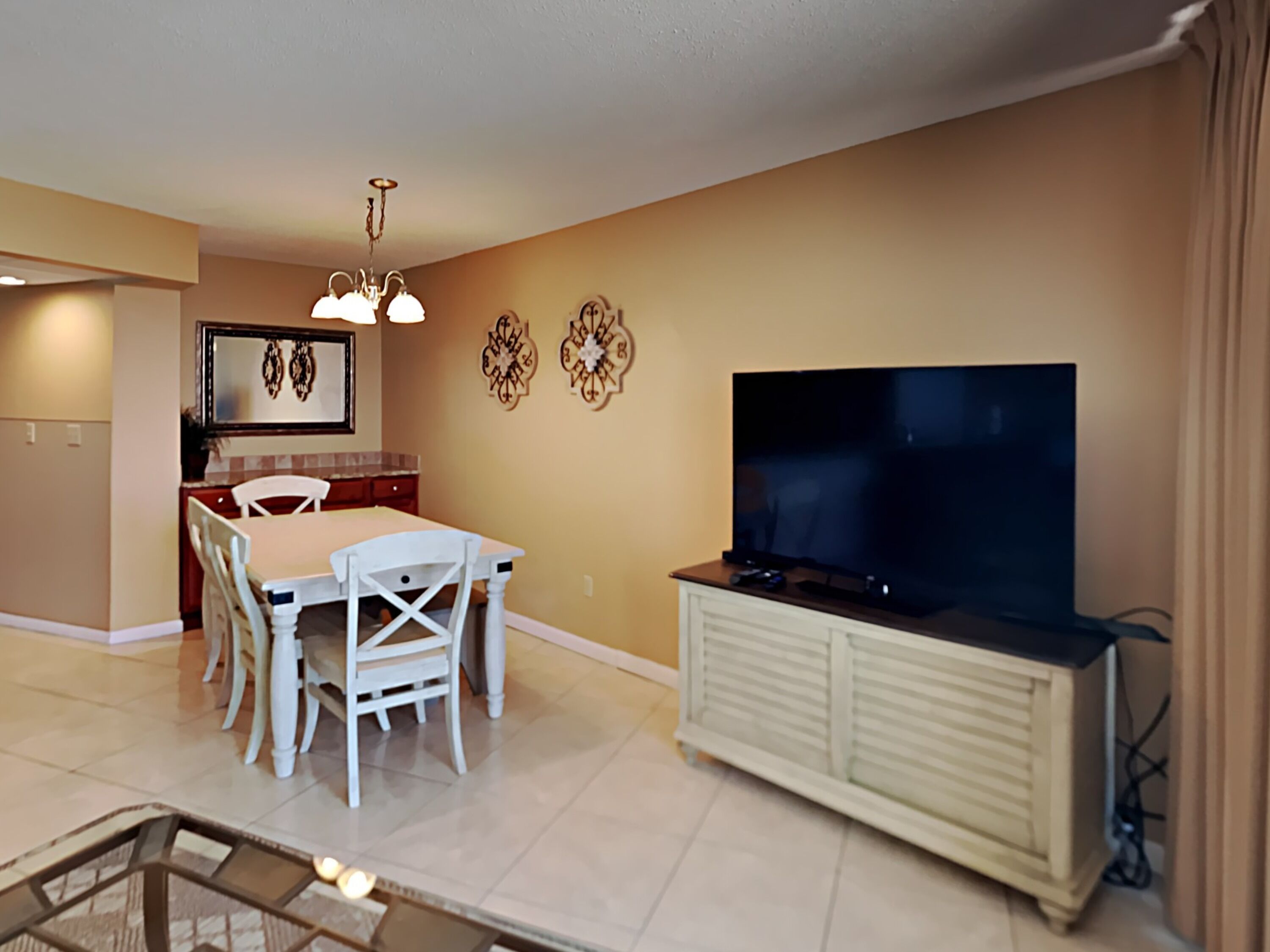A living room with a TV, dining table, chairs, and a kitchen area with a refrigerator.