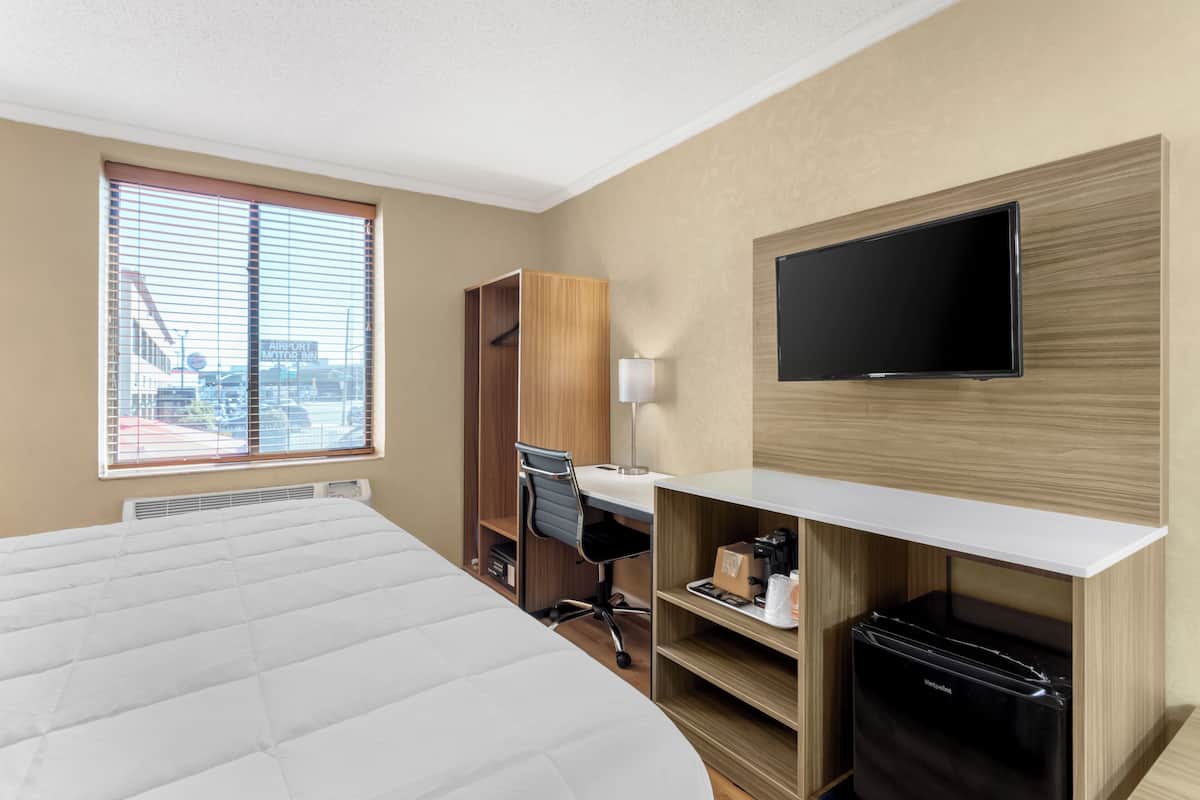 Habitació d'hotel amb llit, escriptori, cadira, televisió i vista a la ciutat per la finestra.