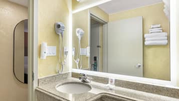 Un baño con encimera de granito, lavamanos, espejo y dos secadores de pelo fijos en la pared.
