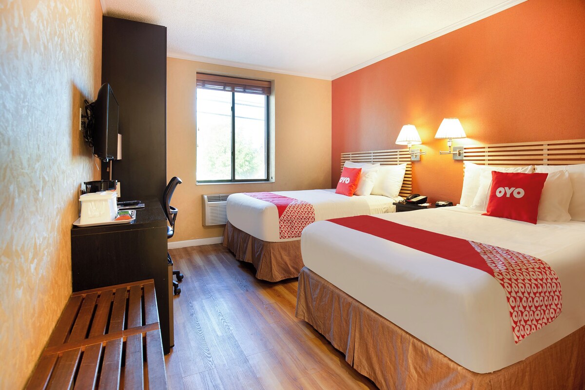 Habitació d'hotel amb dos llits, escriptori, cadira, televisió i finestra.