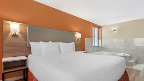 Habitación de hotel con una cama grande, mesitas de noche, cabecero empotrado, lámpara de pared, ventana con persianas y una bañera.