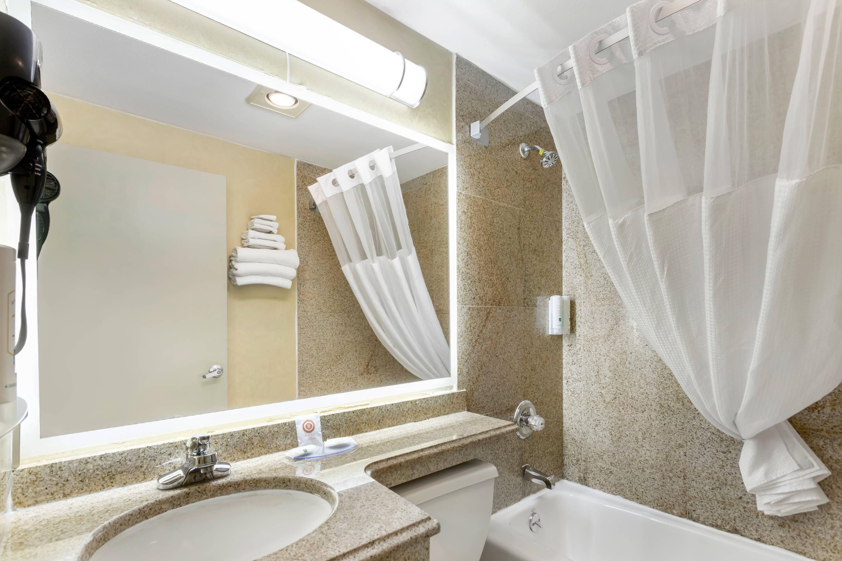 A bathroom with a sink, mirror, shower curtain, and towel rack.