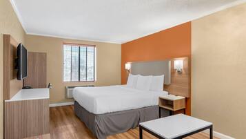 A modern hotel room with a bed, bedside tables, a TV, a window with blinds, and a ceiling light fixture.