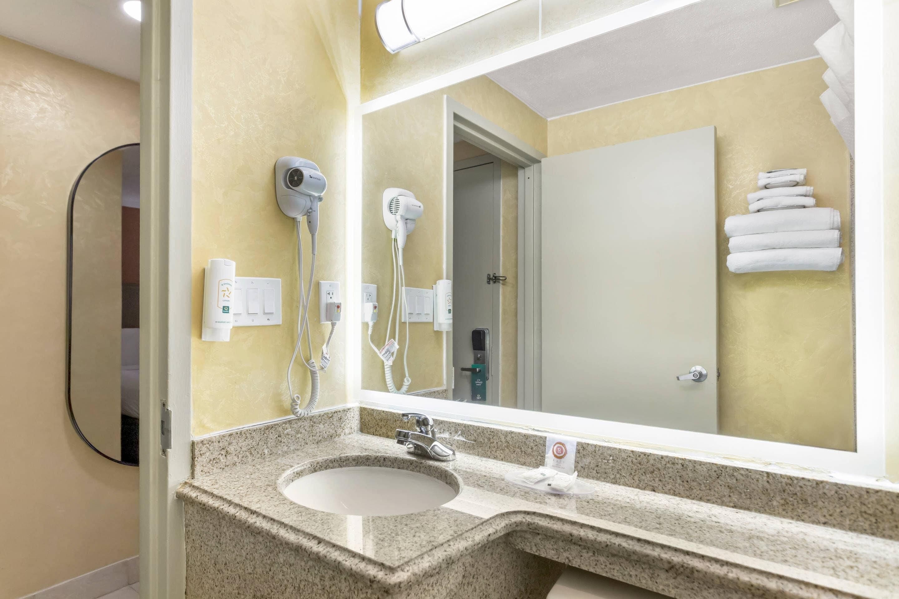 Un baño con encimera de granito, un lavabo, un espejo y dos secadores de pelo fijados en la pared.