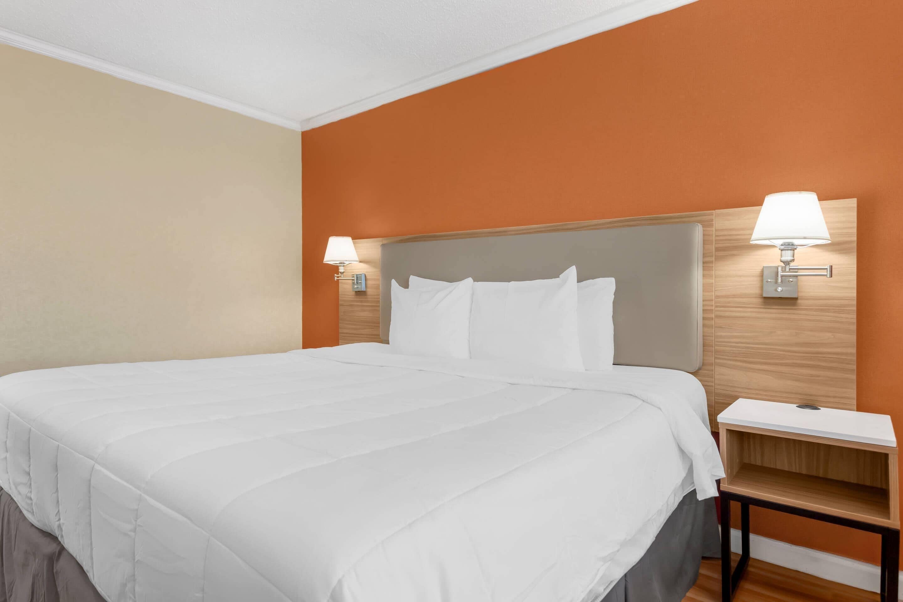 Una habitación de hotel con una cama grande, dos lámparas de noche, una mesita de noche y un cabecero de madera.