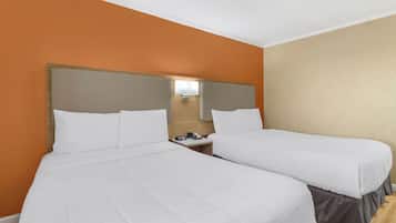 A hotel room with two beds, a wooden headboard, a nightstand, and a wall-mounted lamp.