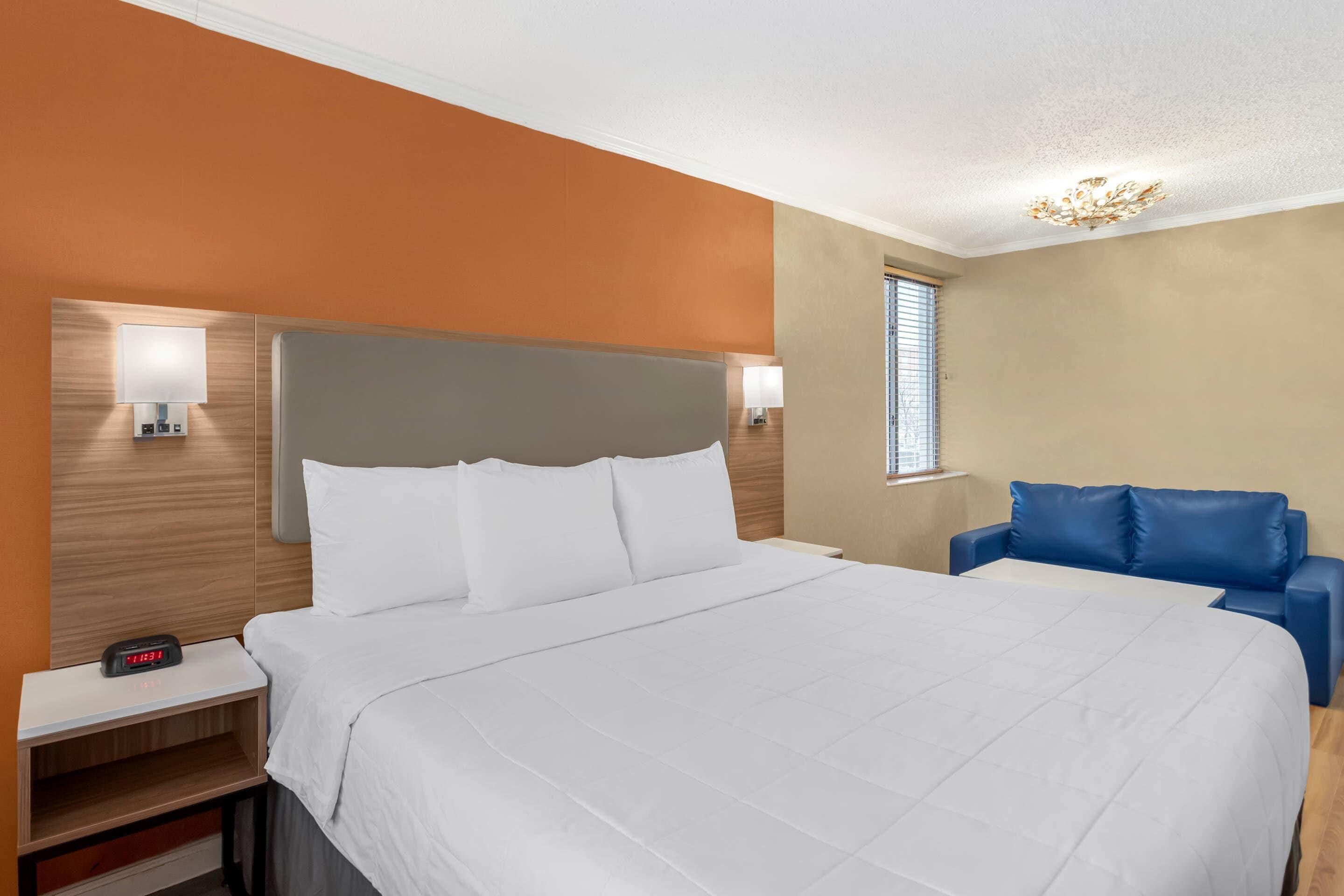 Een hotelkamer met een bed, nachtkastje, lamp en een blauwe fauteuil.
