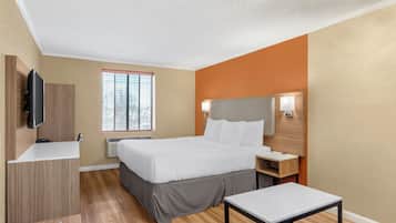 A modern hotel room with a bed, bedside table, TV, and a window with blinds.