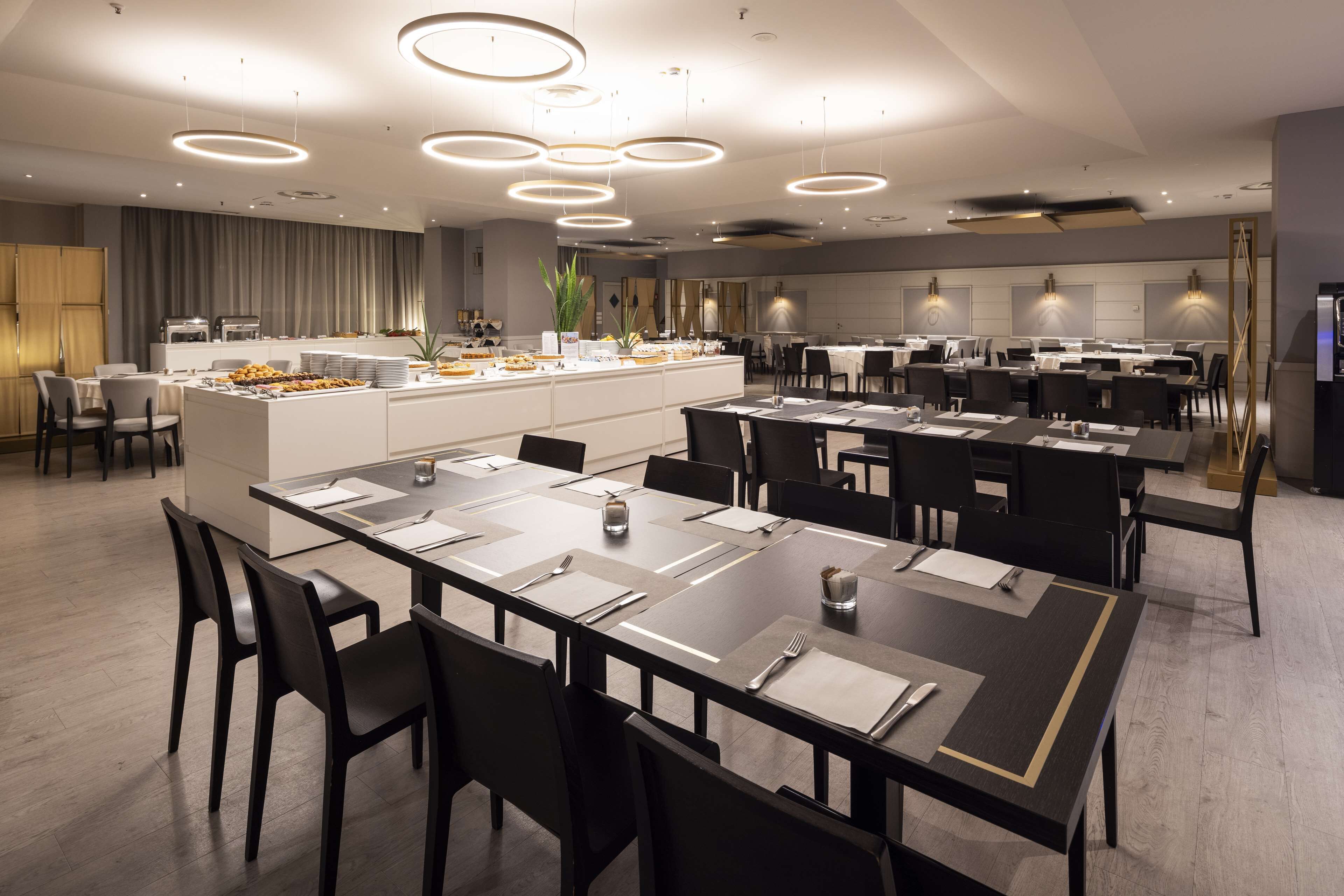A modern dining area with multiple tables and chairs, a central buffet, and contemporary lighting fixtures.