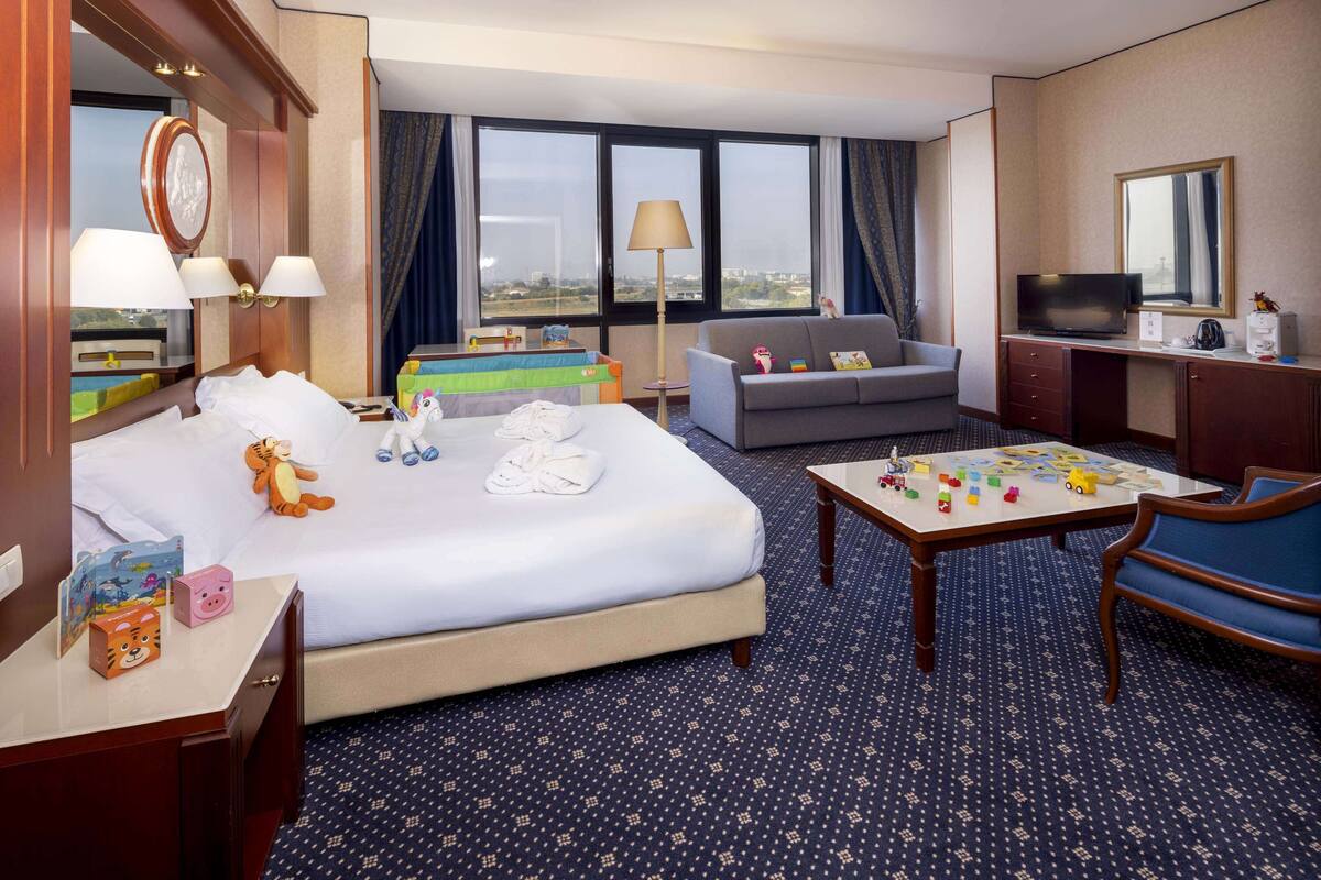 Ein Hotelzimmer mit einem Bett, einer Couch, einem Schreibtisch mit Fernseher und einem Tisch mit Kinderspielzeug.