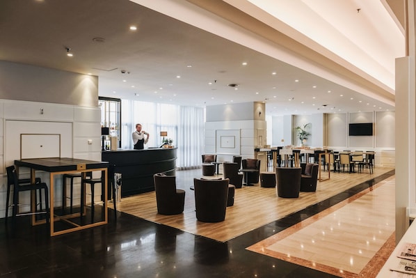 A modern hotel lobby with a bar area, seating arrangements, and a large window providing natural light.
