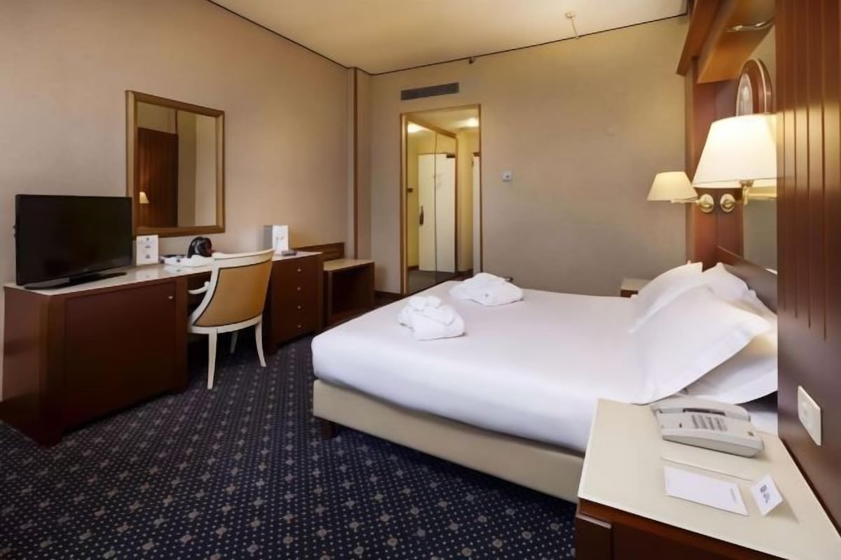 Ett hotellrum med en säng, ett skrivbord med en stol, en tv och en spegel.
