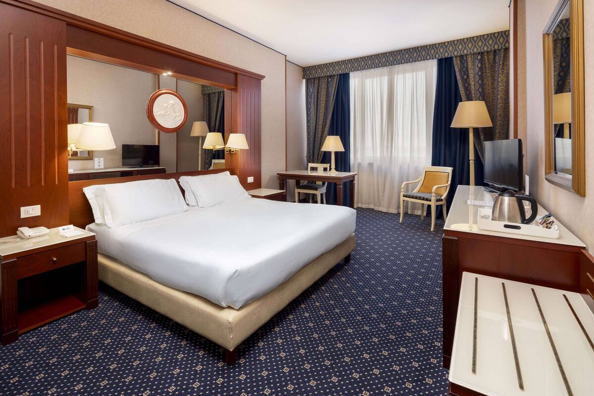 Ein Hotelzimmer mit einem großen Bett, einem Schreibtisch mit Stuhl, einem Fernseher und einem Spiegel.