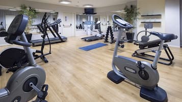Une salle de sport équipée de divers appareils d’exercice, notamment des tapis de course, des vélos elliptiques et des appareils de musculation.
