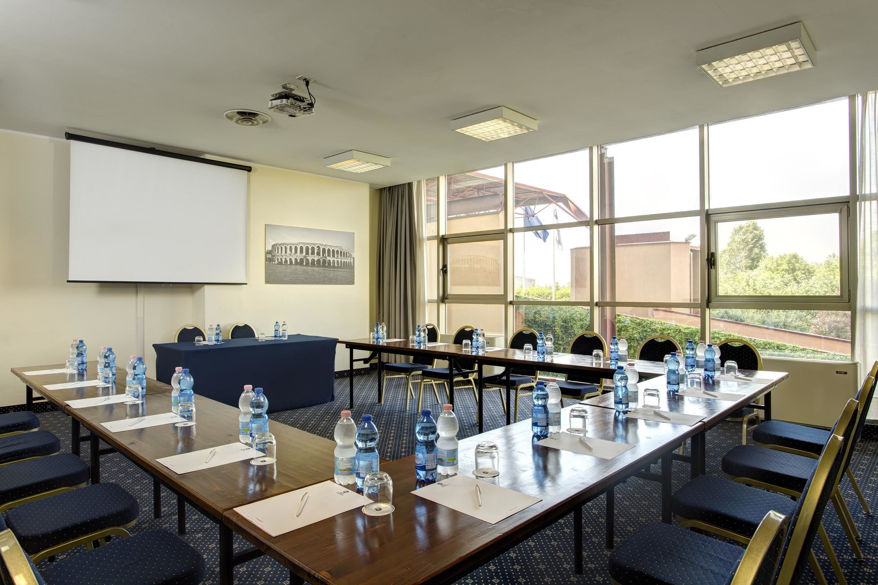 A conference room with a long table, chairs, water bottles, and a projector screen.