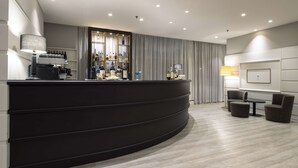 Un espace d’accueil moderne avec un comptoir noir incurvé, une machine à café et un bar bien garni de différentes bouteilles de spiritueux.