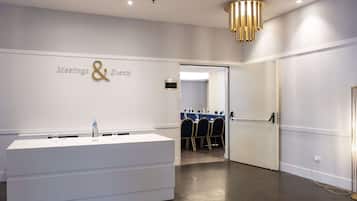 A modern hotel lobby with a reception desk, a 'Meetings & Events' sign, and a conference room visible in the background.