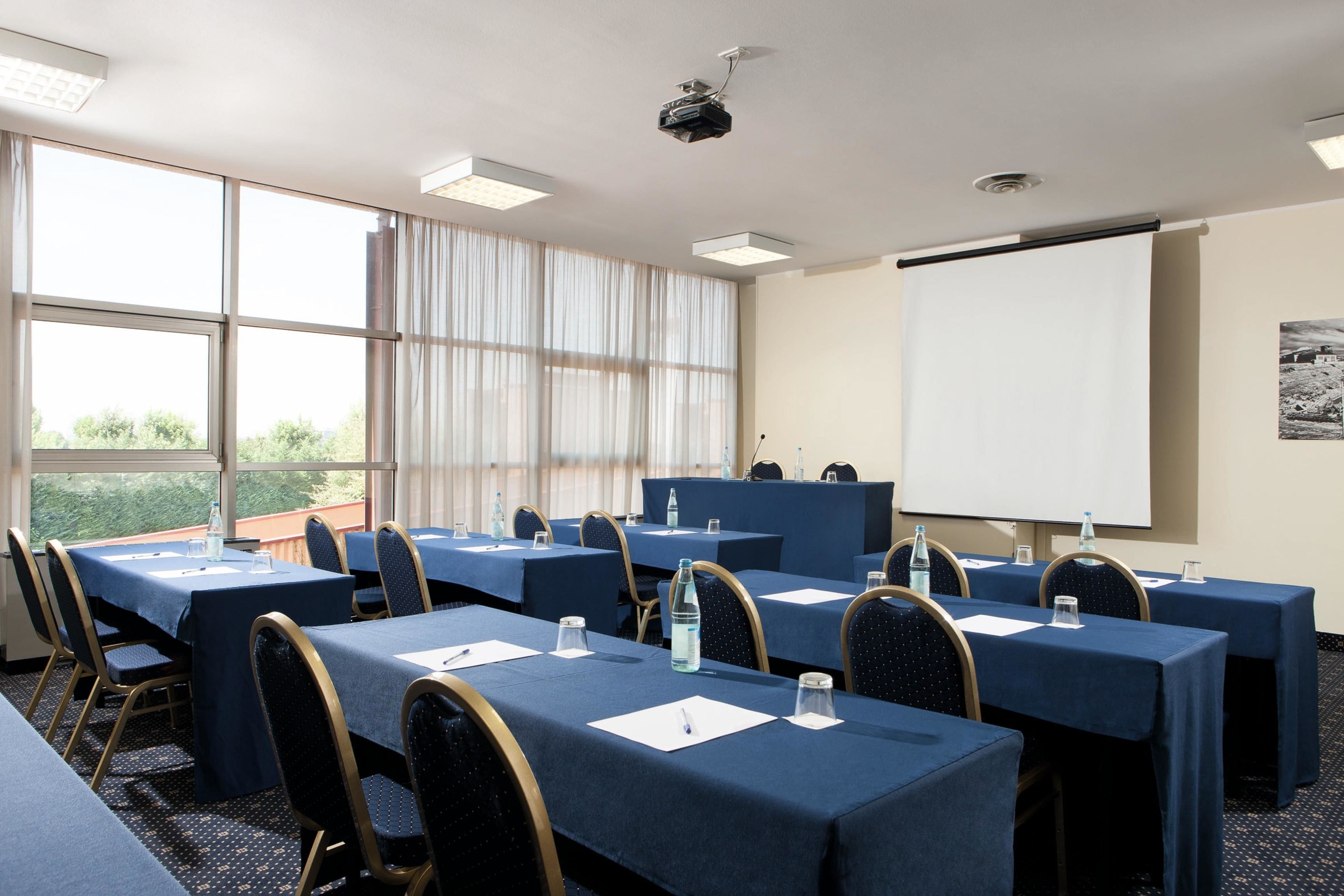 A conference room with tables, chairs, a projector, and a whiteboard.