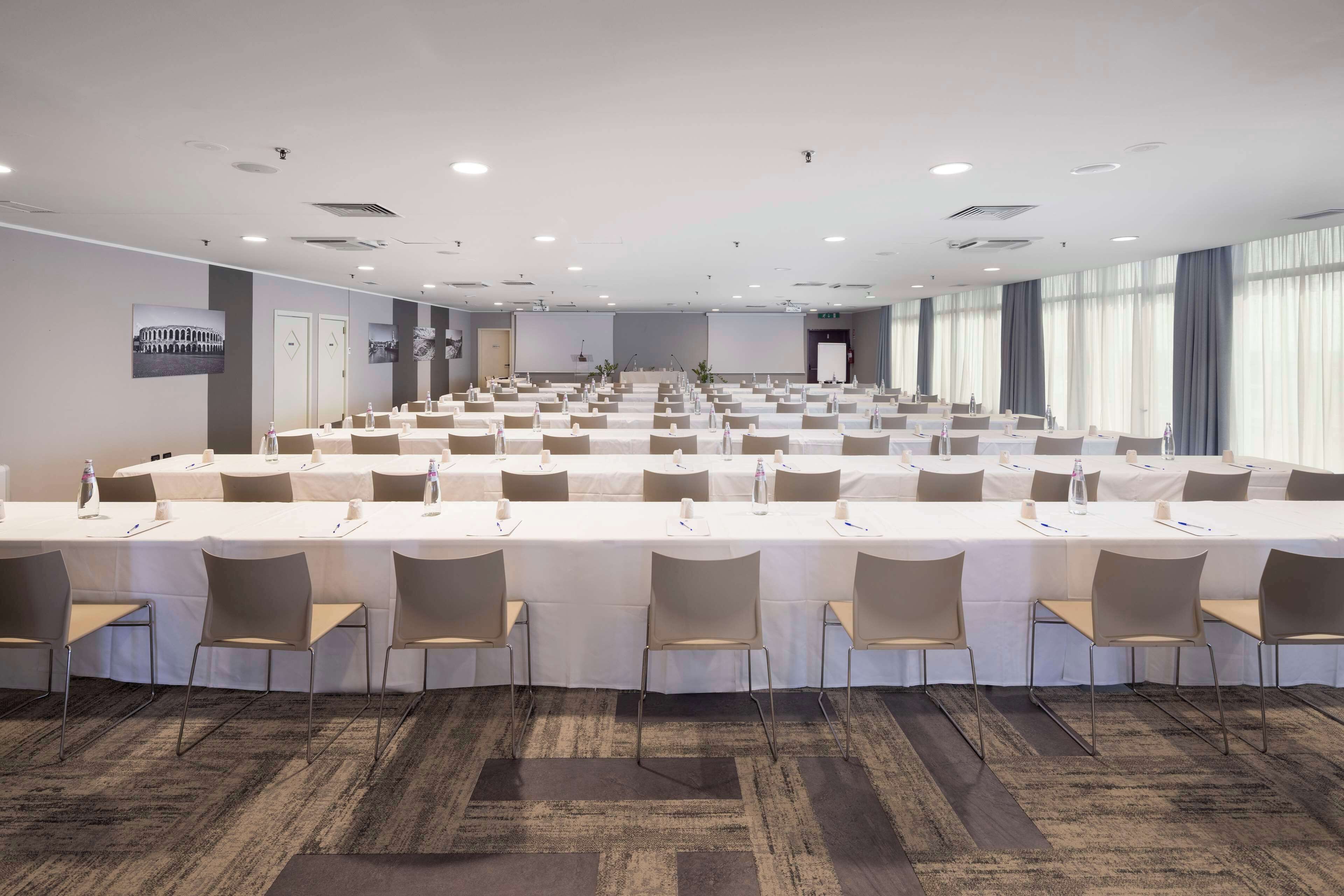 Sala de conferência com várias mesas e cadeiras, equipada com garrafas de água e placas de identificação.
