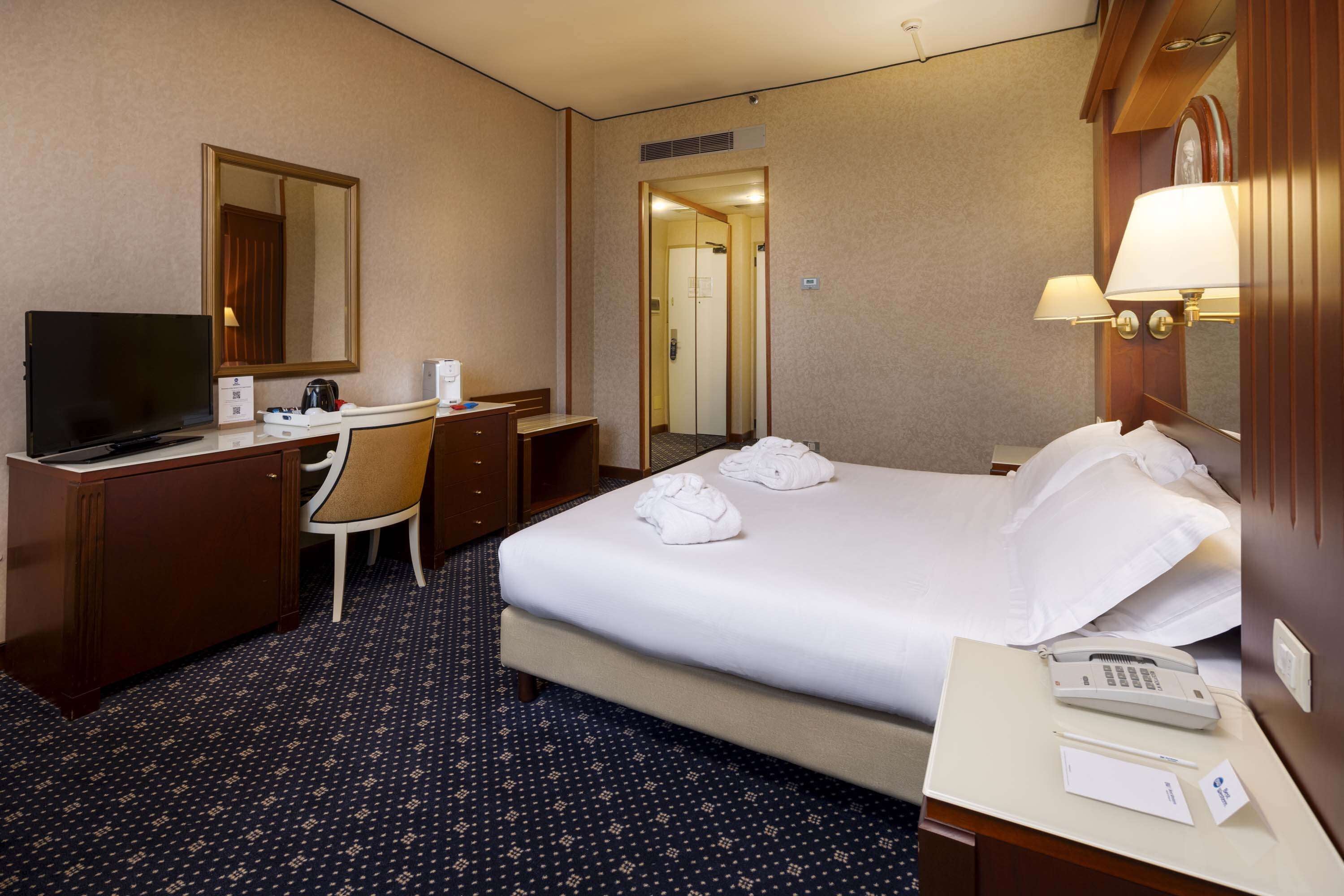 A hotel room with a bed, a desk with a chair, a television, a telephone, and a mirror.
