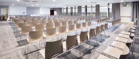 A conference room with rows of chairs and tables, large windows, and a whiteboard.