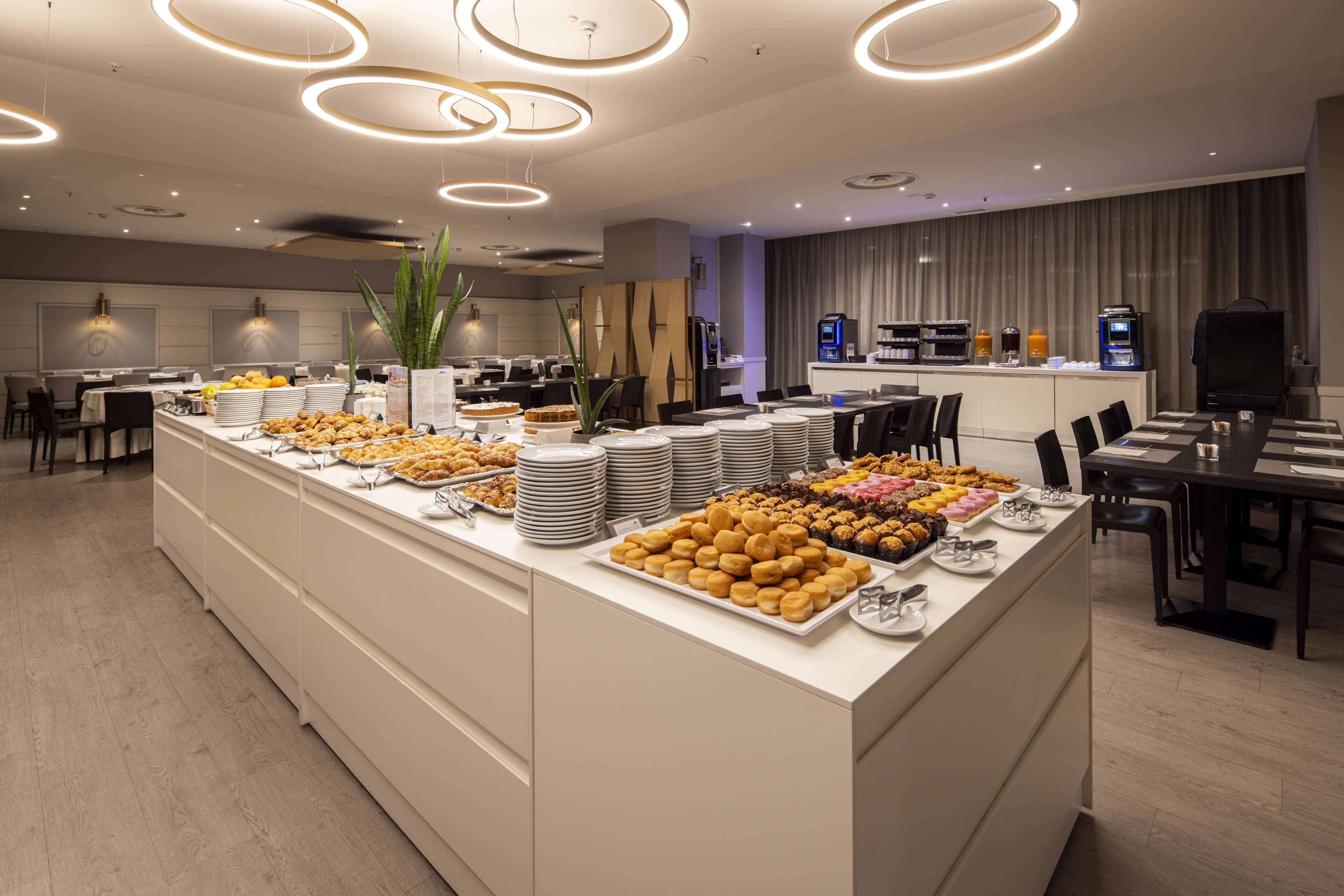 A modern hotel dining area with a buffet setup, including various food items and a coffee station.
