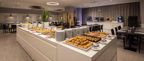 A modern hotel dining area with a buffet setup, including various food items and a coffee station.