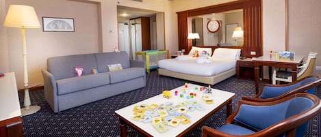 Habitación de hotel con sofá, cama, mesa de comedor y juguetes infantiles, además de un espejo.