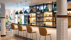 A modern bar area with a curved counter, bar stools, and pendant lighting. - Hotel München City Center affiliated by Meliá (Munich)