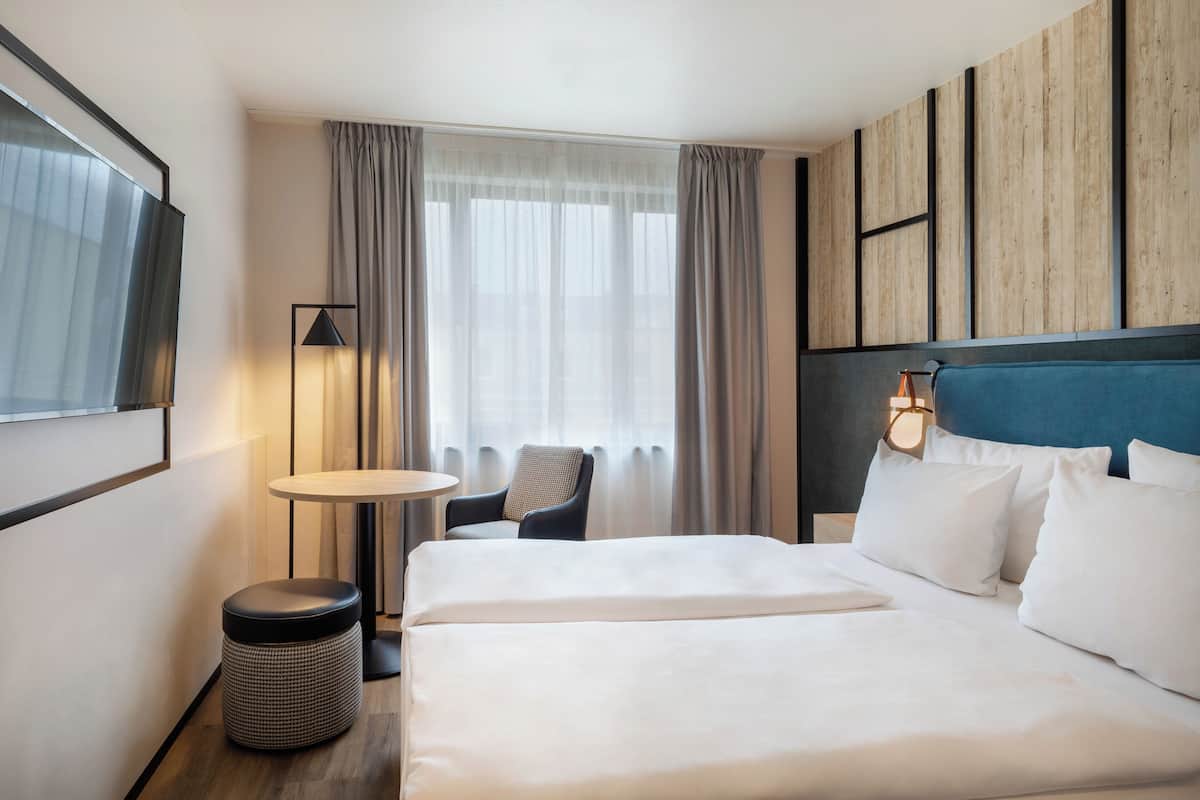 A hotel room with a large bed, a chair, a small table, and a TV mounted on the wall.