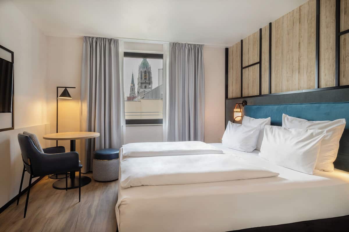 A hotel room with a bed, a chair, a small table, and a lamp.