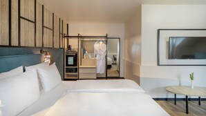 A modern hotel room with a large bed, a seating area with a table, a TV mounted on the wall, and a wardrobe with a mirror. - Hotel München City Center affiliated by Meliá (Munich)